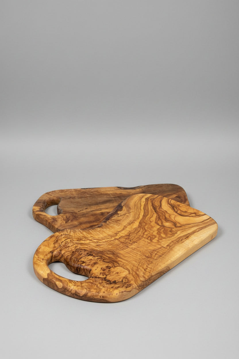 Two handcrafted olive wood serving boards with natural live-edge shapes and cutout handles, displayed on a wooden tabletop.
