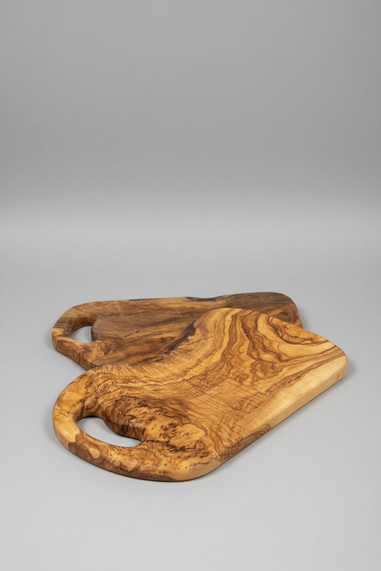 Two handcrafted olive wood serving boards with natural live-edge shapes and cutout handles, displayed on a wooden tabletop.