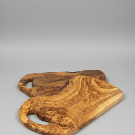 Two handcrafted olive wood serving boards with natural live-edge shapes and cutout handles, displayed on a wooden tabletop.