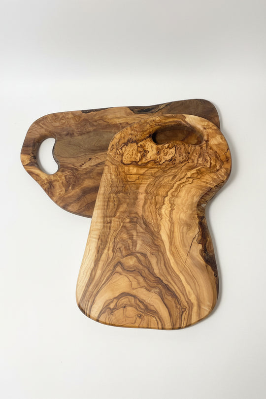 Two handcrafted olive wood cutting boards with natural live edges and grain patterns, displayed on a light wood floor.
