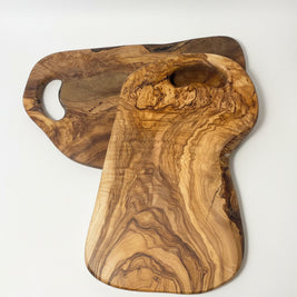 Two handcrafted olive wood cutting boards with natural live edges and grain patterns, displayed on a light wood floor.