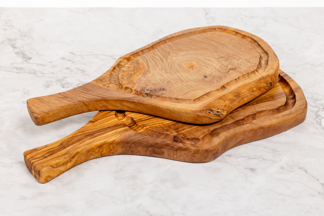 Two rustic olive wood serving boards with handles, stacked on a white marble surface.