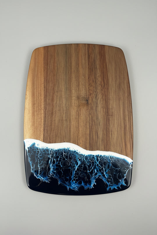 Wooden cutting board with a blue and black resin design on a gray background