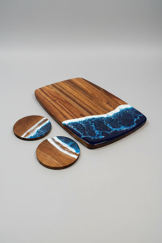 A wooden serving board and two matching round coasters with an ocean wave design in blue, white, and tan, arranged on a burlap-textured background.