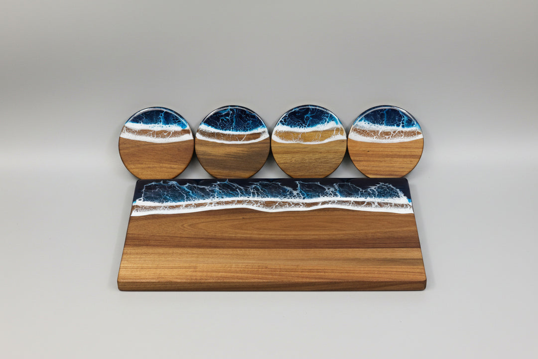 A rectangular wooden board and four round coasters featuring an ocean wave design with brown wood grain, white foam, and deep blue water, displayed on a beige woven fabric surface.