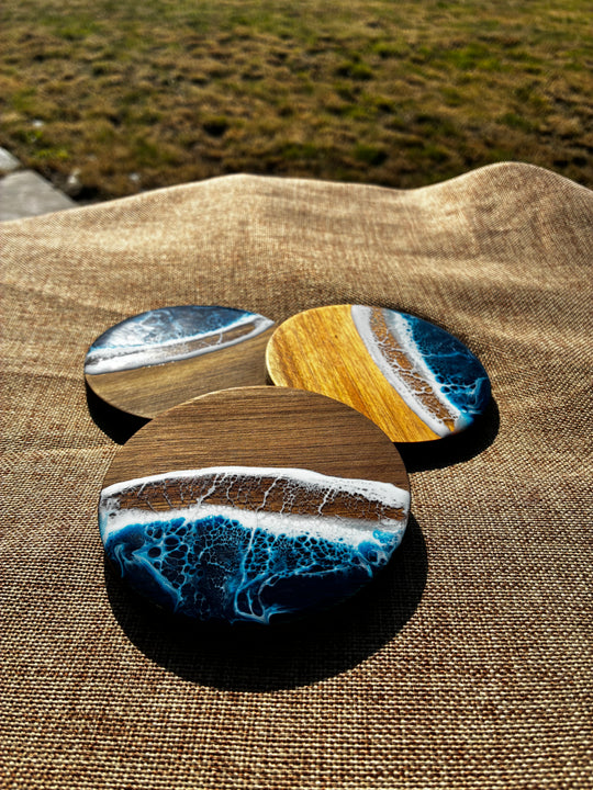 Three round coasters with a resin ocean wave design resting on a brown burlap fabric outdoors.