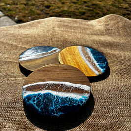 Three round coasters with a resin ocean wave design resting on a brown burlap fabric outdoors.