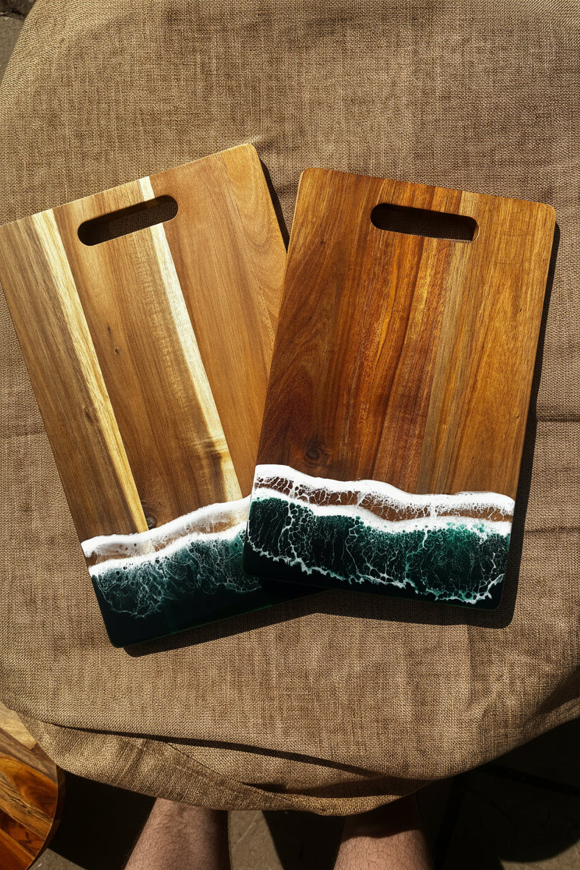Two wooden cutting boards with ocean wave designs in the lower half, displayed on a textured brown fabric surface.