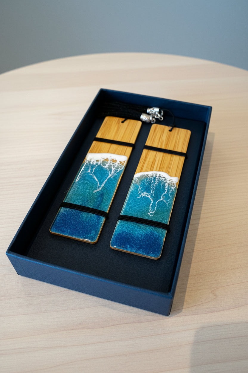 A pair of rectangular drop earrings displayed in a dark blue gift box on a light wood table. The earrings feature a natural bamboo wood top half with a blue and white resin bottom half depicting ocean waves, connected by a silver-toned metal clasp.