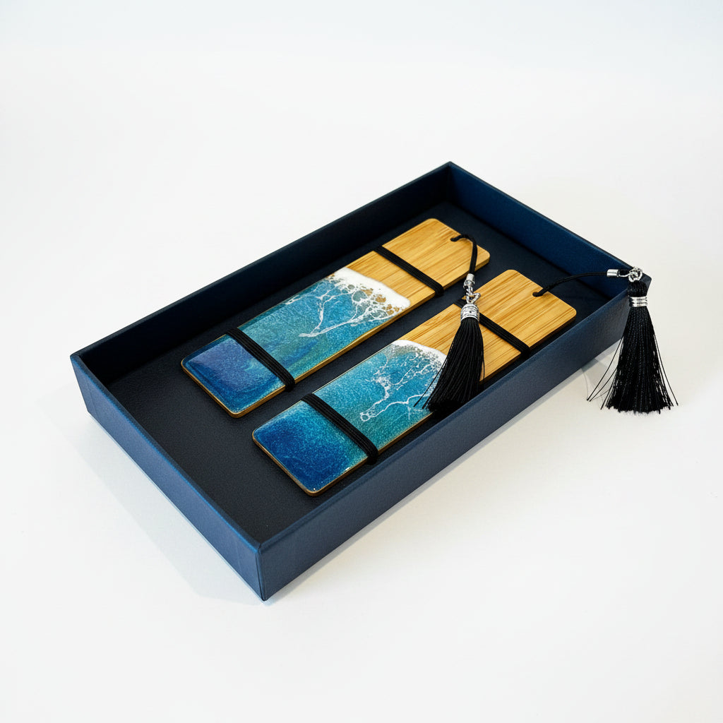 A boxed set of two rectangular wooden bookmarks or tags with blue ocean wave artwork, black bands, and black tassels, displayed inside a dark navy presentation box on a white background.