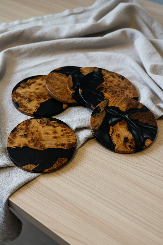 Four round coasters with a black and natural burl wood grain pattern, arranged on a light wood table draped with a beige linen cloth.