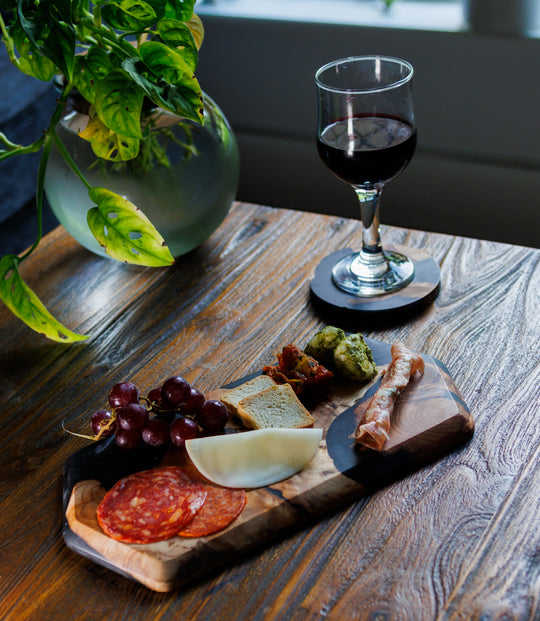 Wooden platter with cured meats, cheese, and grapes next to a glass of red wine on a wooden table.