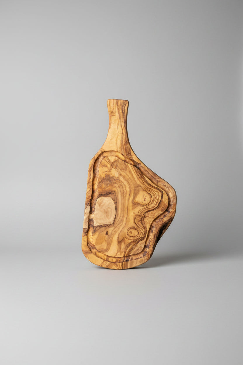 A rustic live-edge wooden serving board with a natural irregular shape and rich wood grain, displayed on a light brown wooden floor alongside other matching wooden decor pieces.