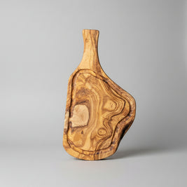 A rustic live-edge wooden serving board with a natural irregular shape and rich wood grain, displayed on a light brown wooden floor alongside other matching wooden decor pieces.