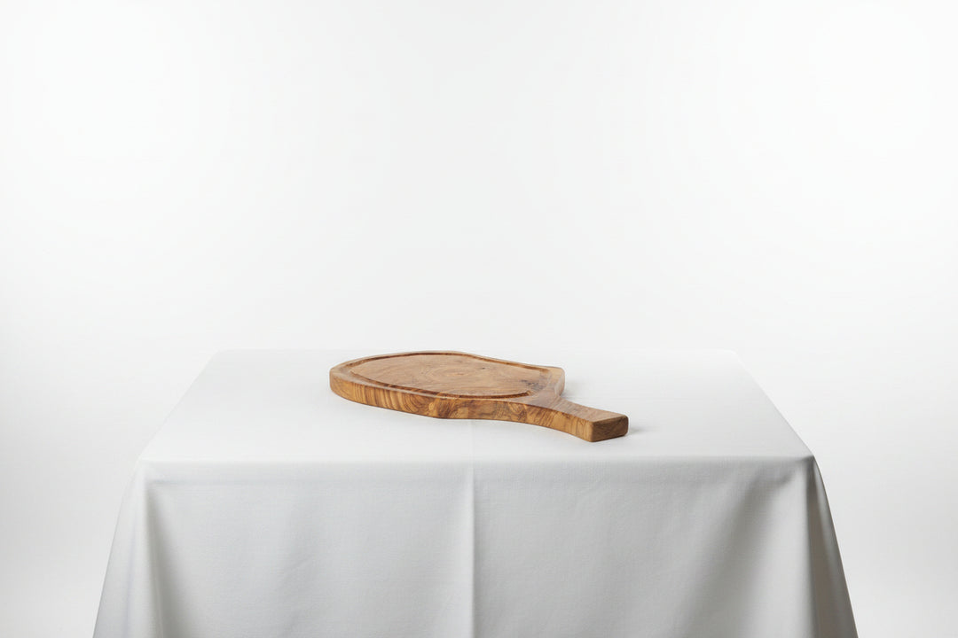 A small oval wooden serving board with a handle, resting on a white tablecloth against a white studio background.