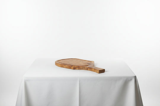 A small oval wooden serving board with a handle, resting on a white tablecloth against a white studio background.
