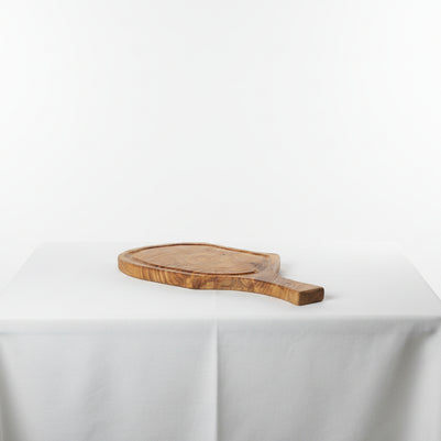 A small oval wooden serving board with a handle, resting on a white tablecloth against a white studio background.