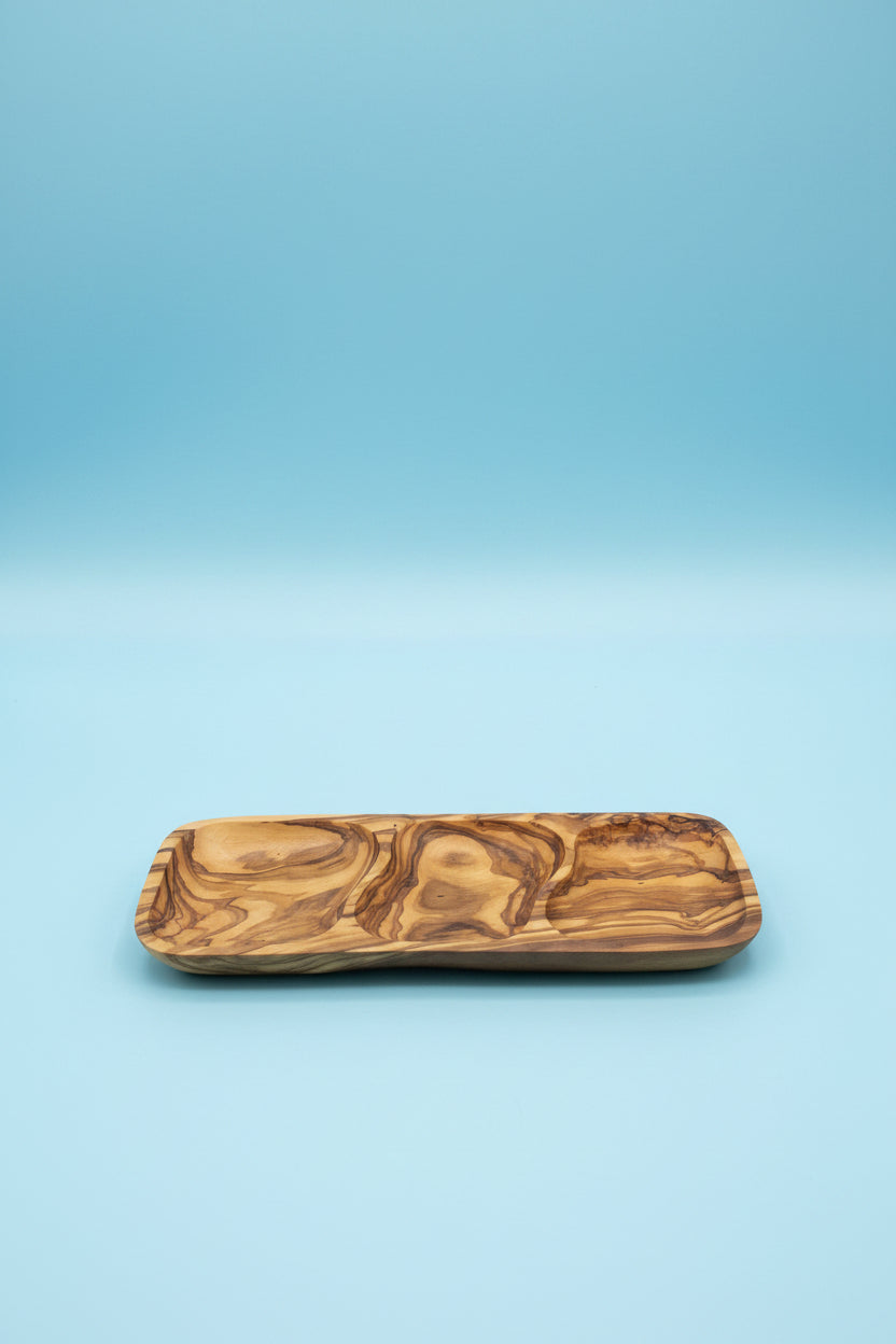 A rectangular wooden serving tray with a carved, swirling natural wood grain pattern, resting on a light brown wooden table.