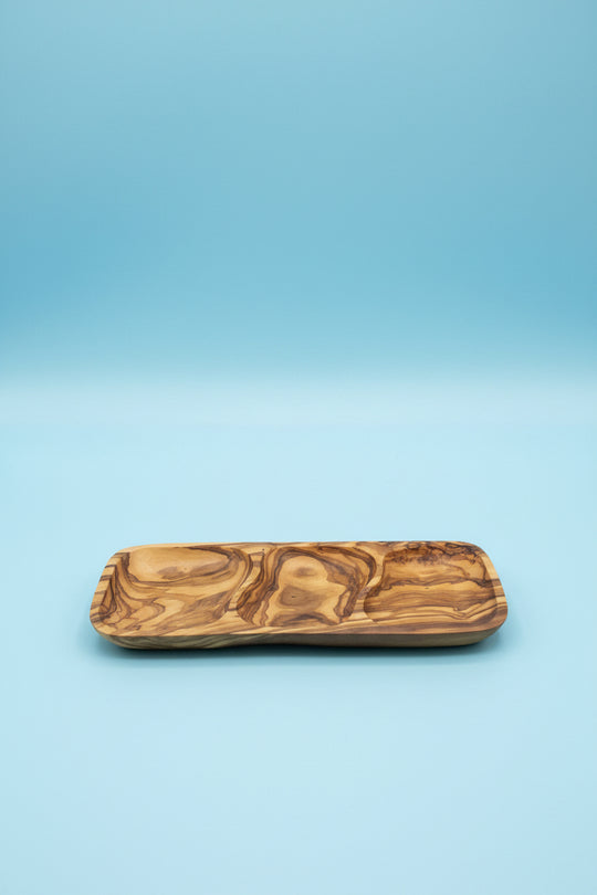 A rectangular wooden serving tray with a carved, swirling natural wood grain pattern, resting on a light brown wooden table.