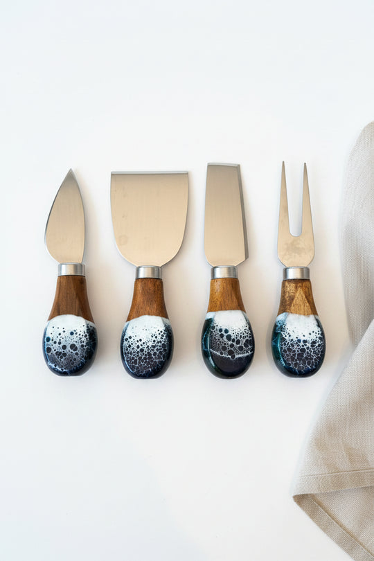 Four cheese knives and a fork with polished steel blades and marbled resin handles in brown, black, and white, arranged on a brown burlap surface.