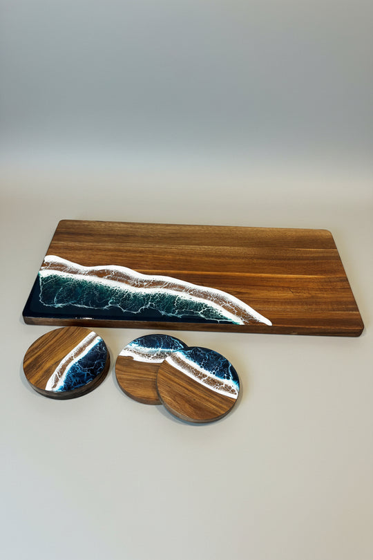 A wooden serving board and three matching coasters with an ocean wave pattern in dark blue, teal, and white, displayed on a textured beige tablecloth.